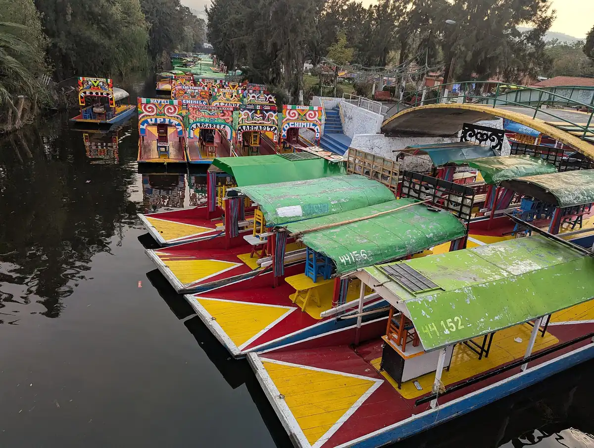 Painted trajineras moored at a Xochimilco embarcadero in Mexico City, where a boat costs MX$750 an hour shared by the group